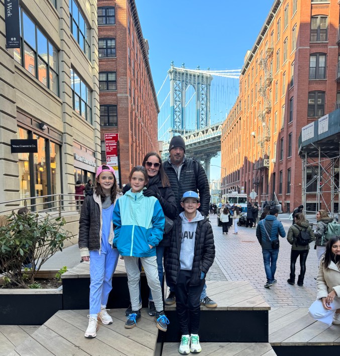 Family standing in DUMBO Brooklyn with Manhattan Bridge in the background in New York City with kids
