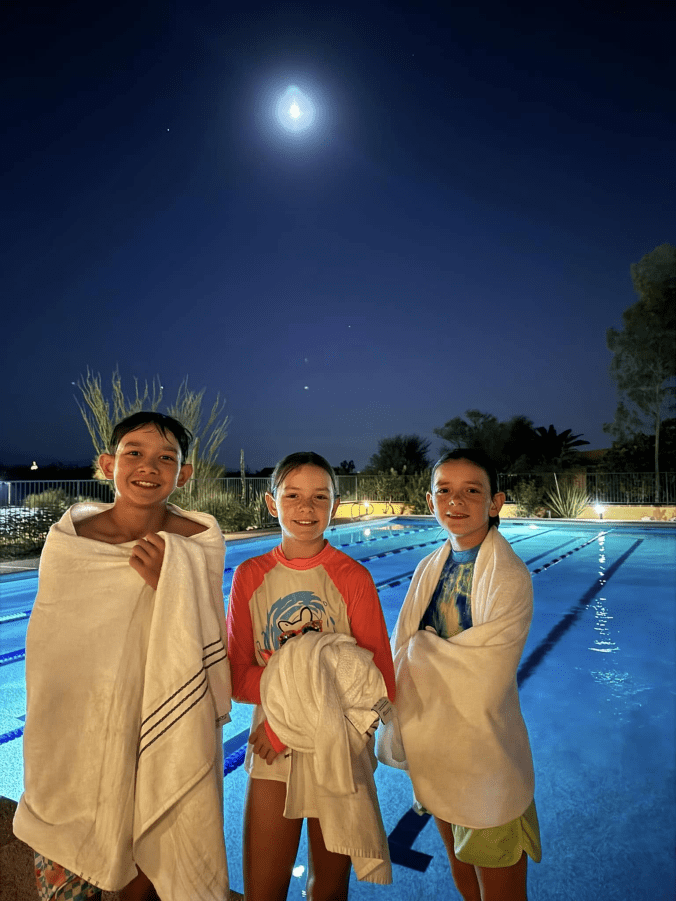 Kids wrapped in towels relaxing by a pool at night after a long day of travel
