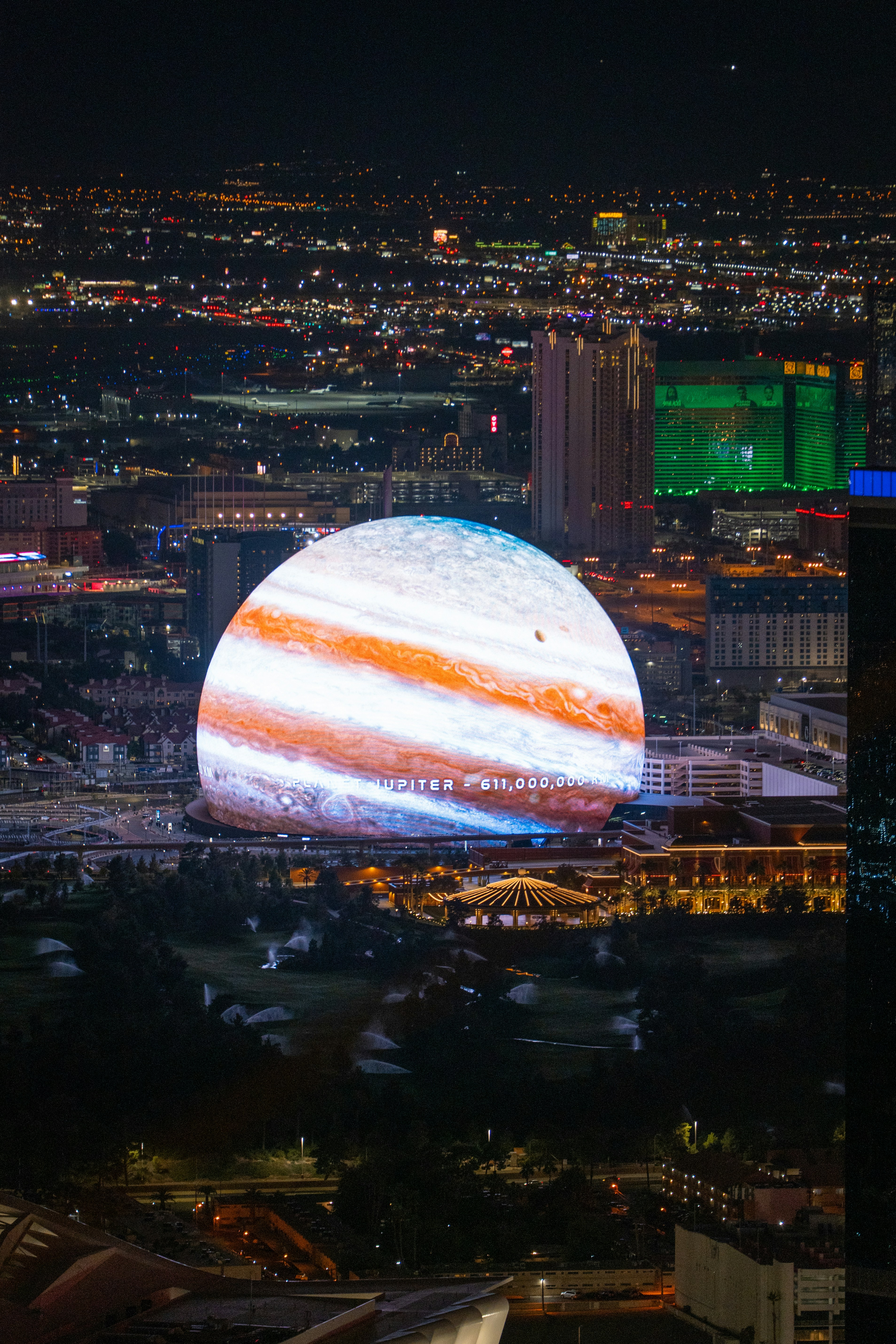 Las Vegas Sphere lit up at night resembling planet Jupiter above the Las Vegas skyline