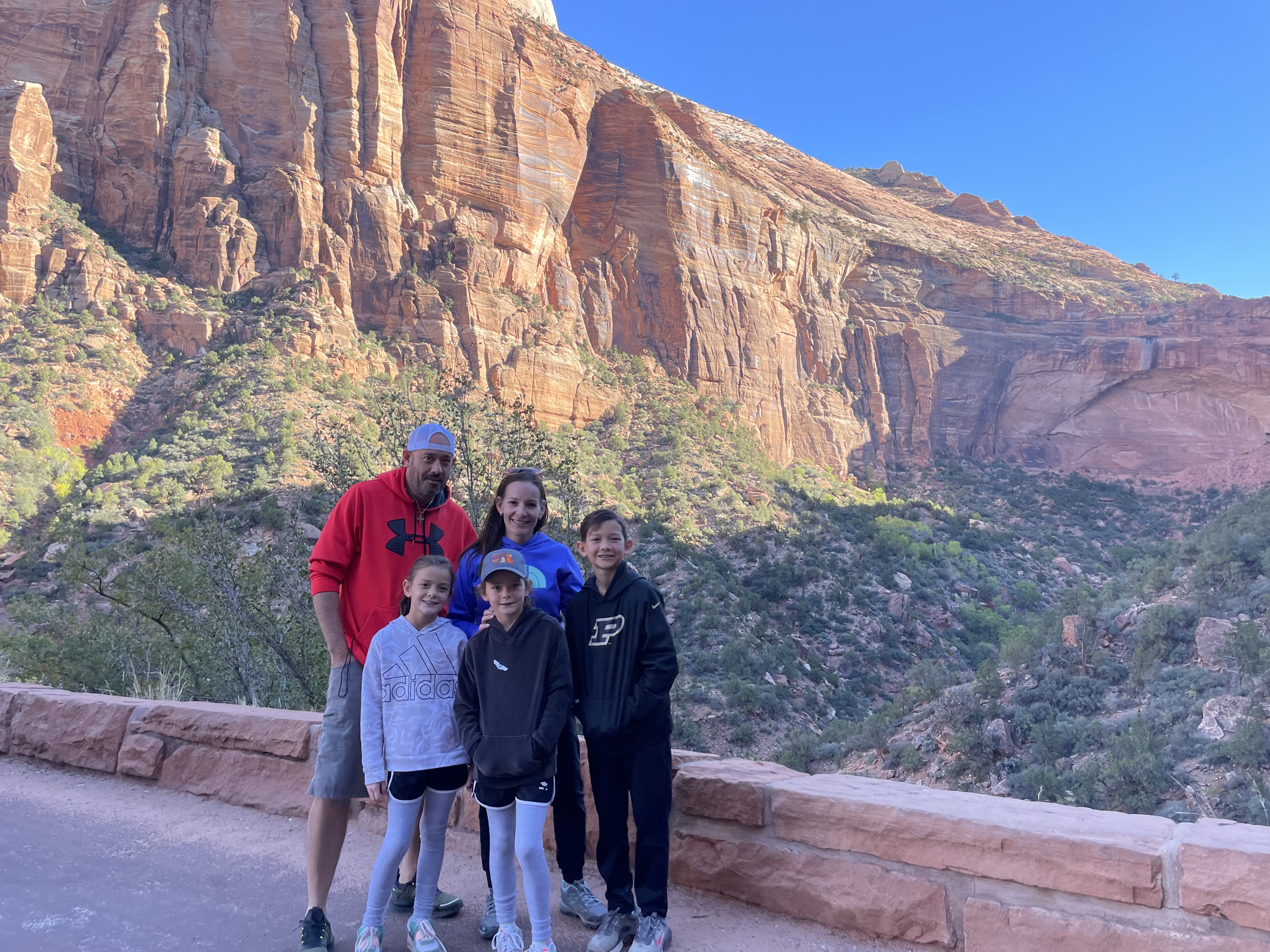 Family standing together with Zion National Park canyon cliffs in the background