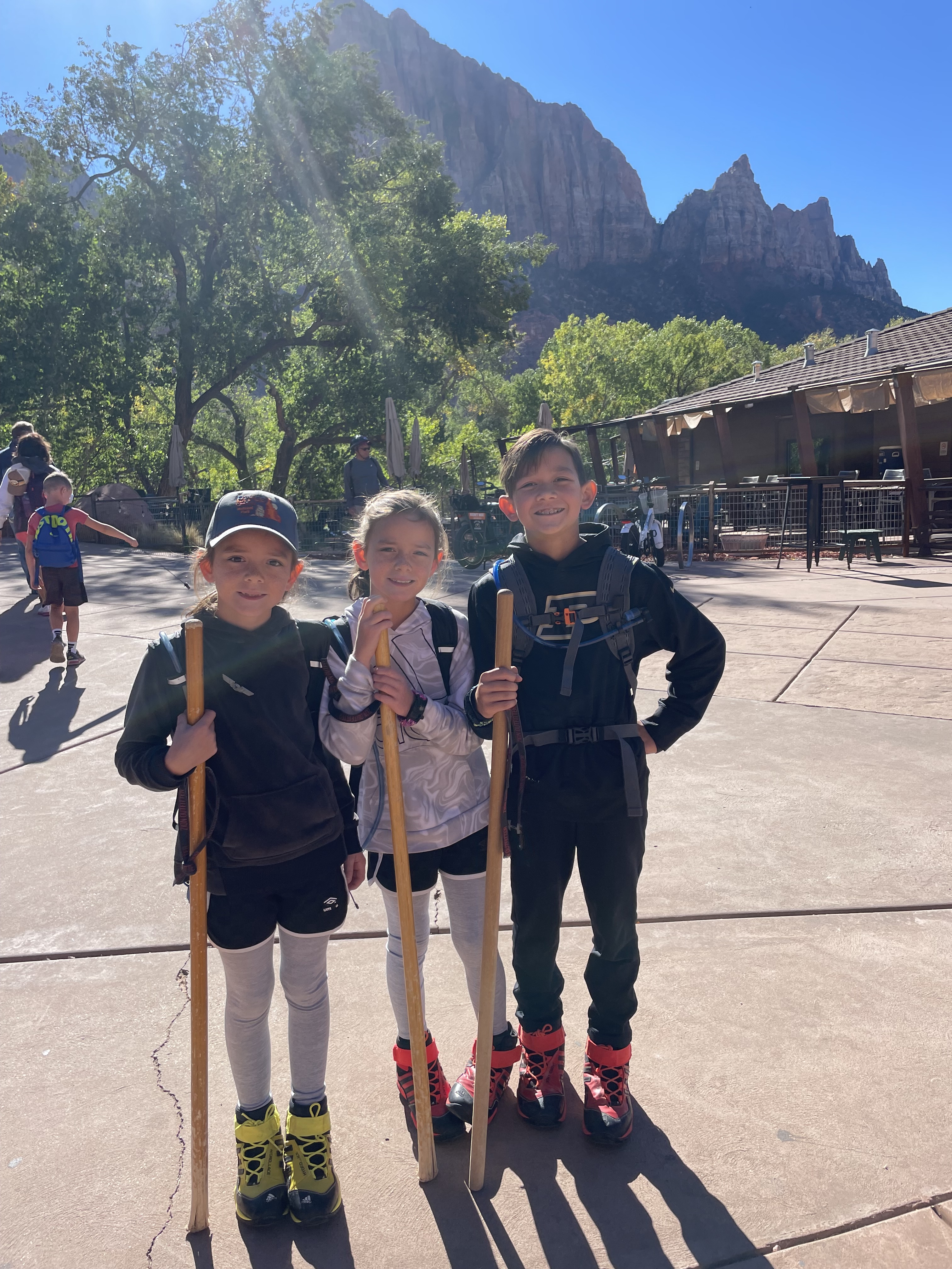 Kids holding walking sticks and wearing rented hiking gear before hiking The Narrows in Zion