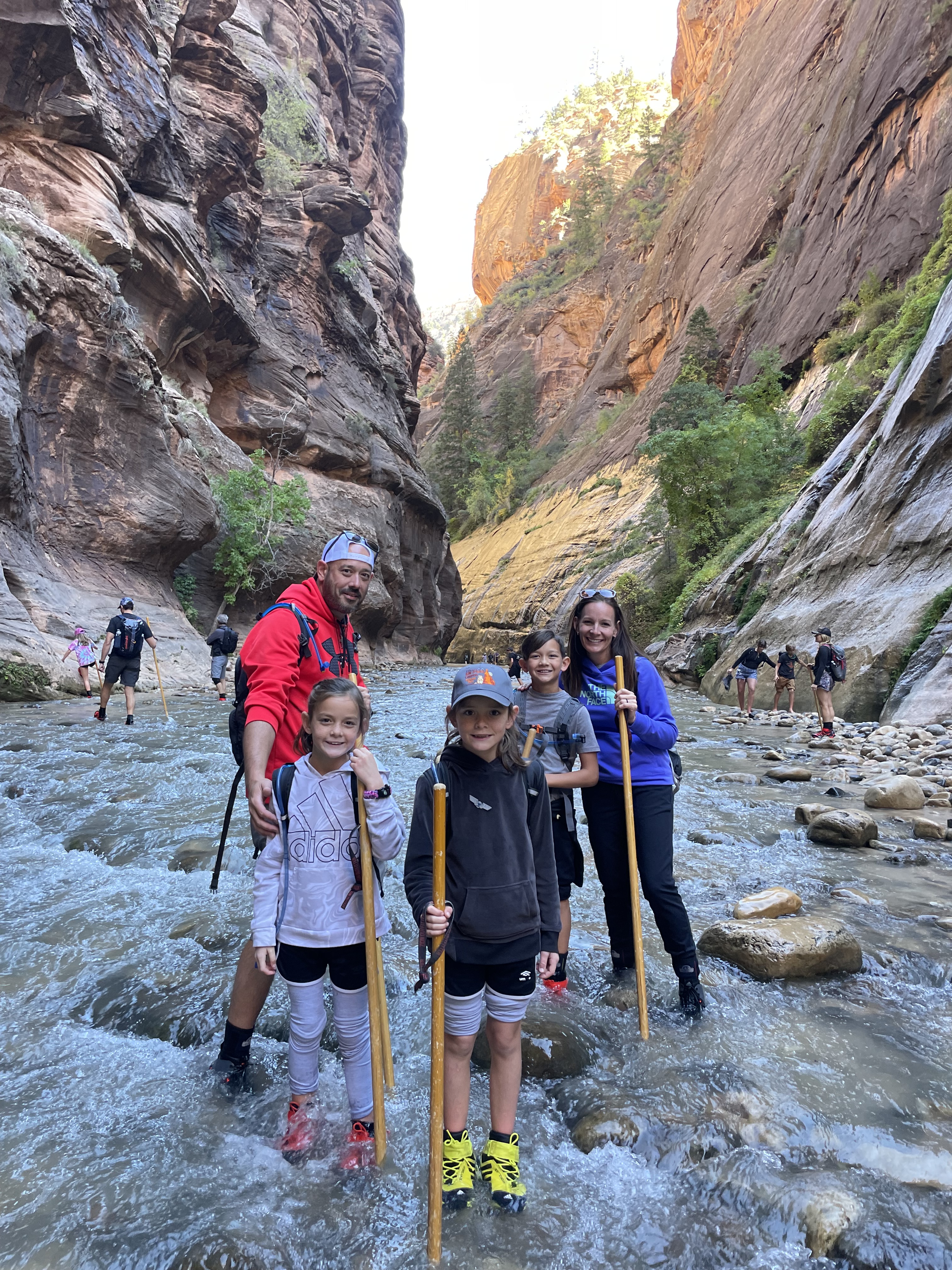 Family hiking The Narrows in Zion National Park with walking sticks and water hiking shoes