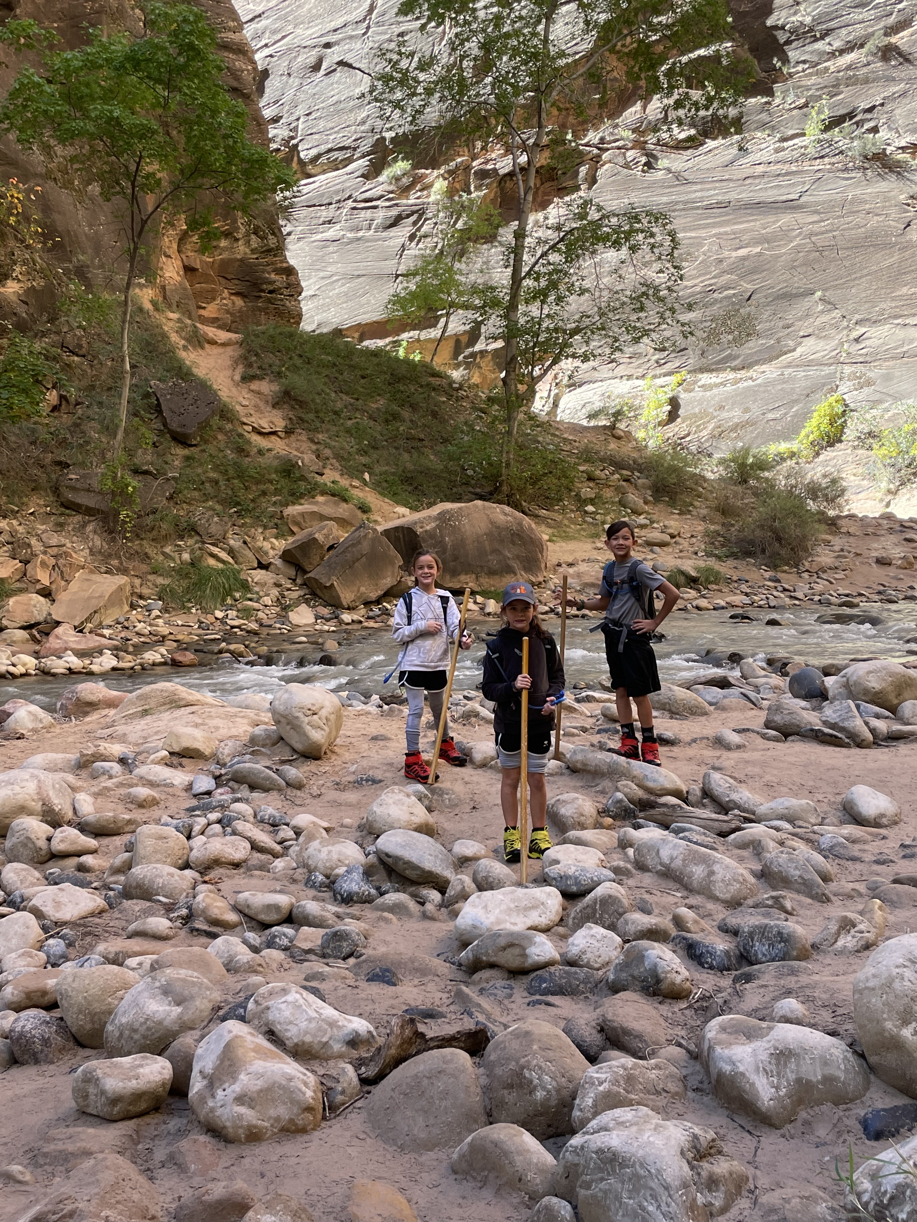 Kids standing on rocks with walking sticks during The Narrows hike in Zion National Park