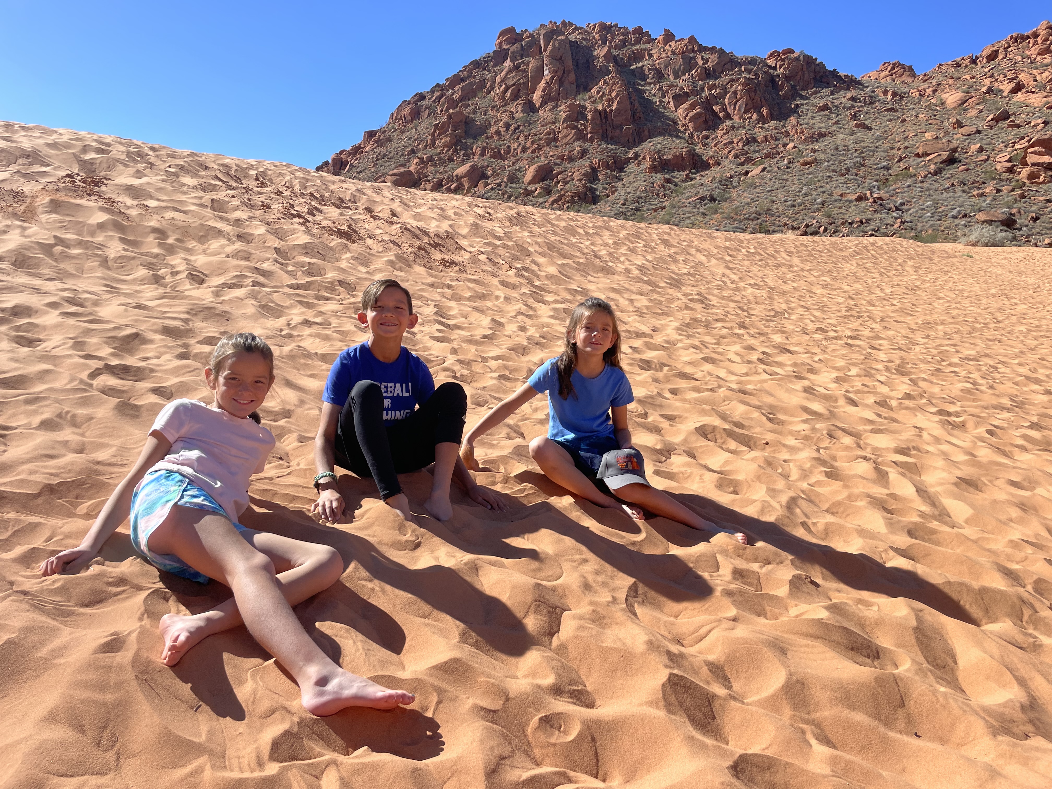 Kids sitting and playing in the red sand dunes at Snow Canyon State Park