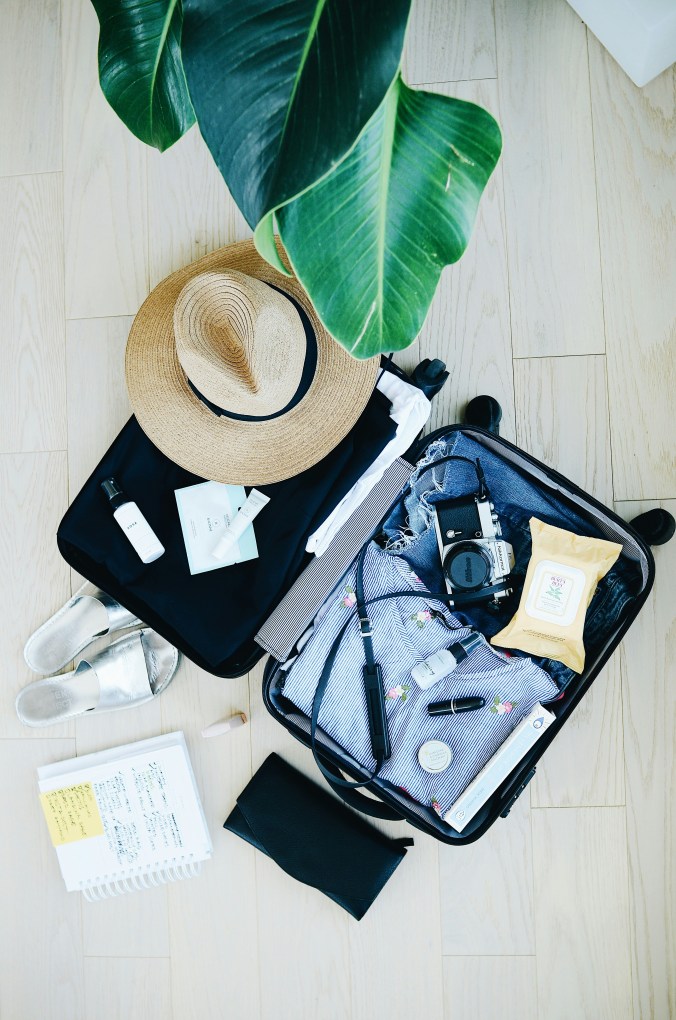 Open suitcase with neatly packed travel essentials including clothes, camera, toiletries, and straw hat for a family trip