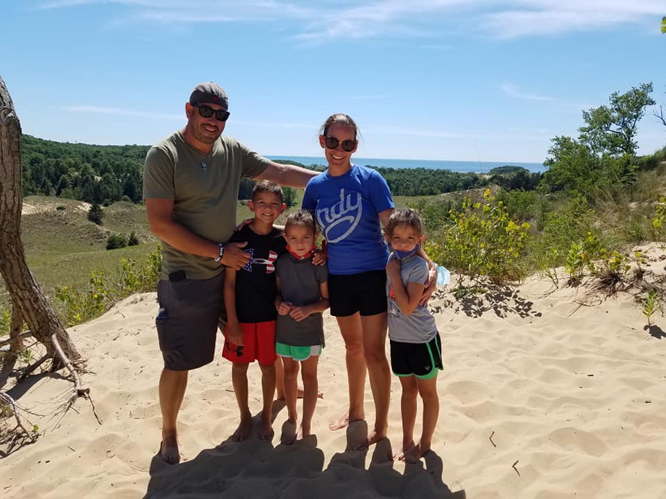Family standing barefoot in the sand dunes near Saugatuck, Michigan with rolling dunes and Lake Michigan in the background.