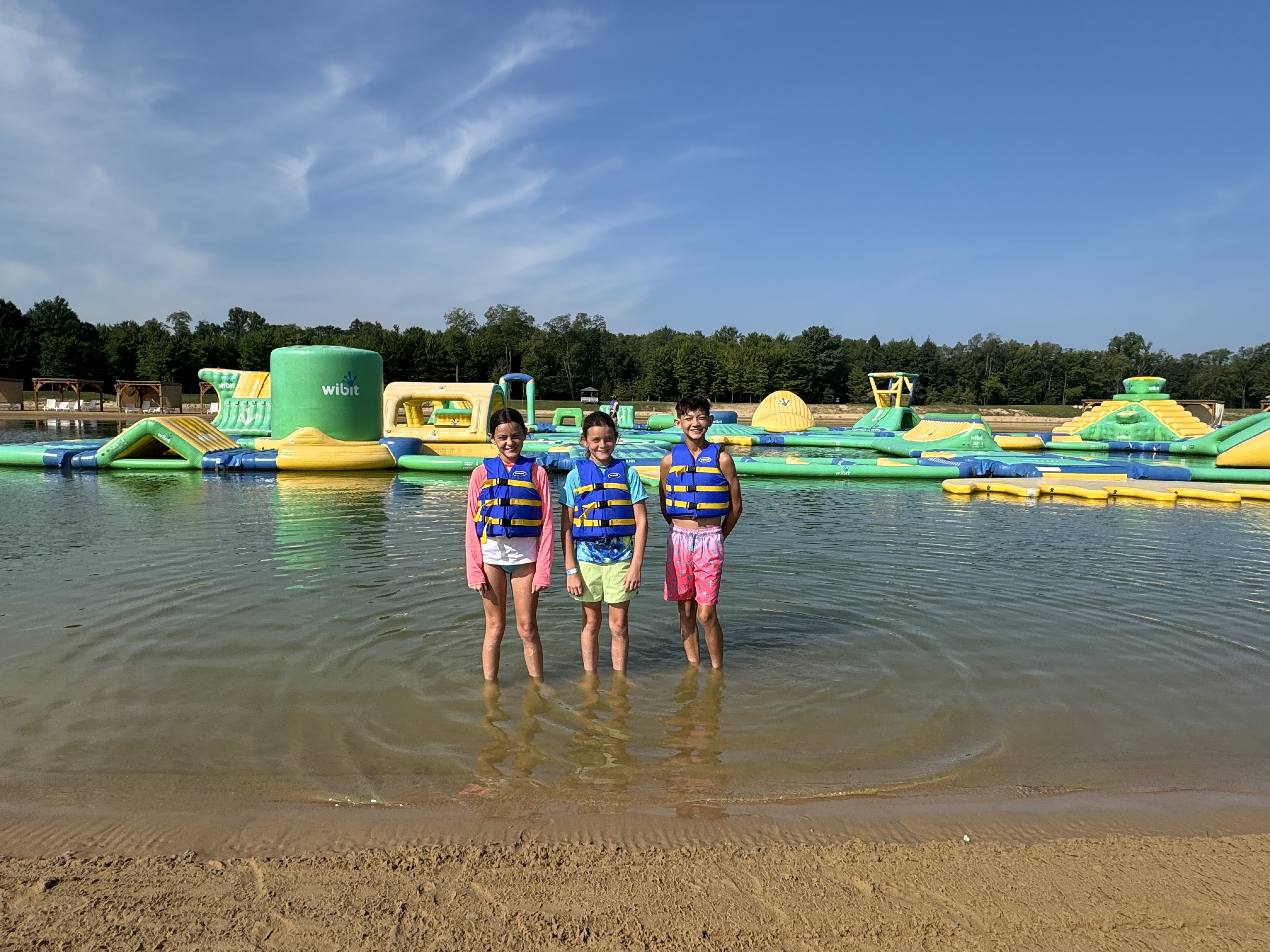 Lake Arvesta Farms Family Fun Kids standing in shallow water in front of the inflatable water park at Lake Arvesta Farms.