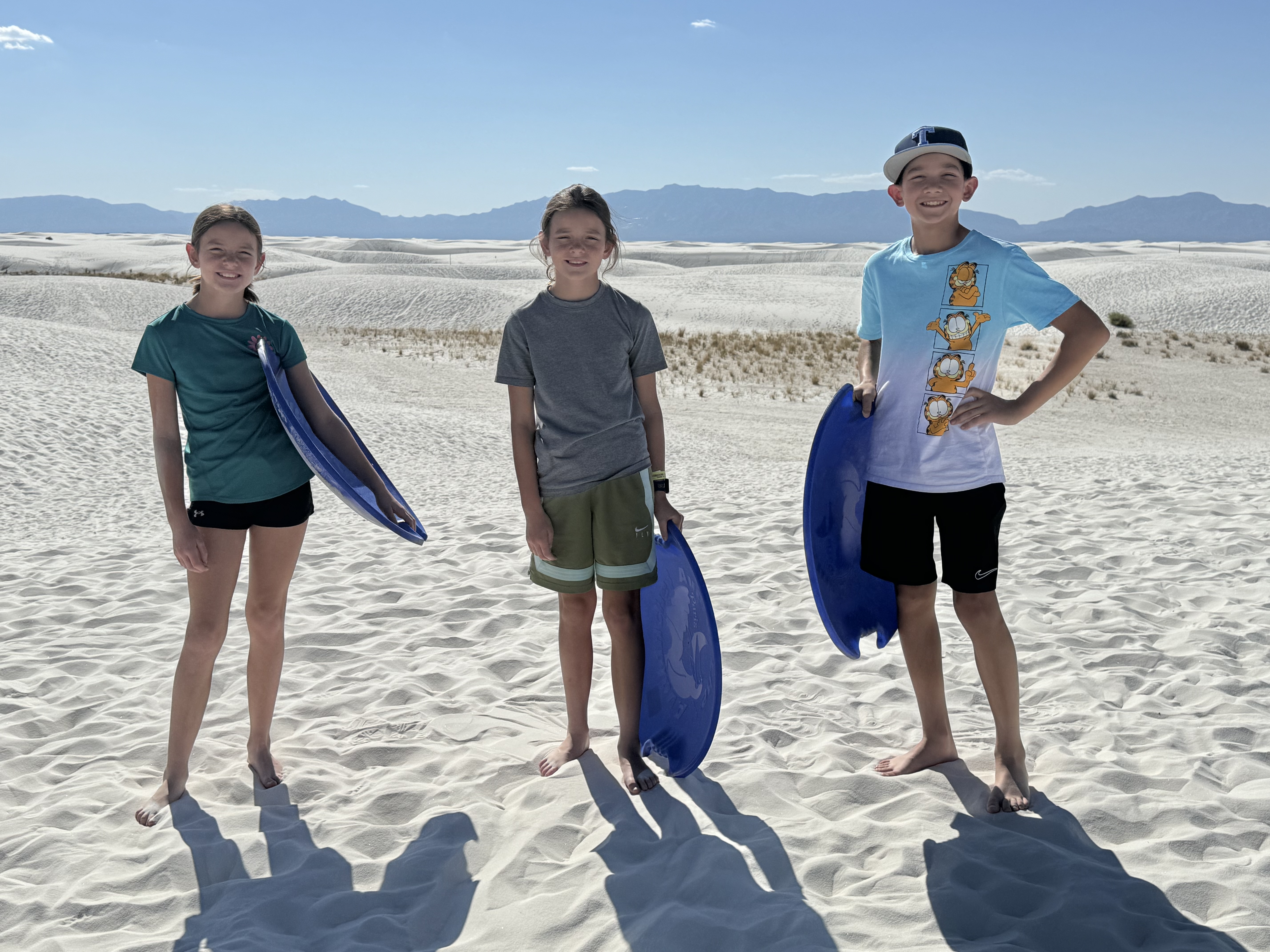 Kids holding sleds at White Sands National Park in New Mexico with white dunes and mountains in the background