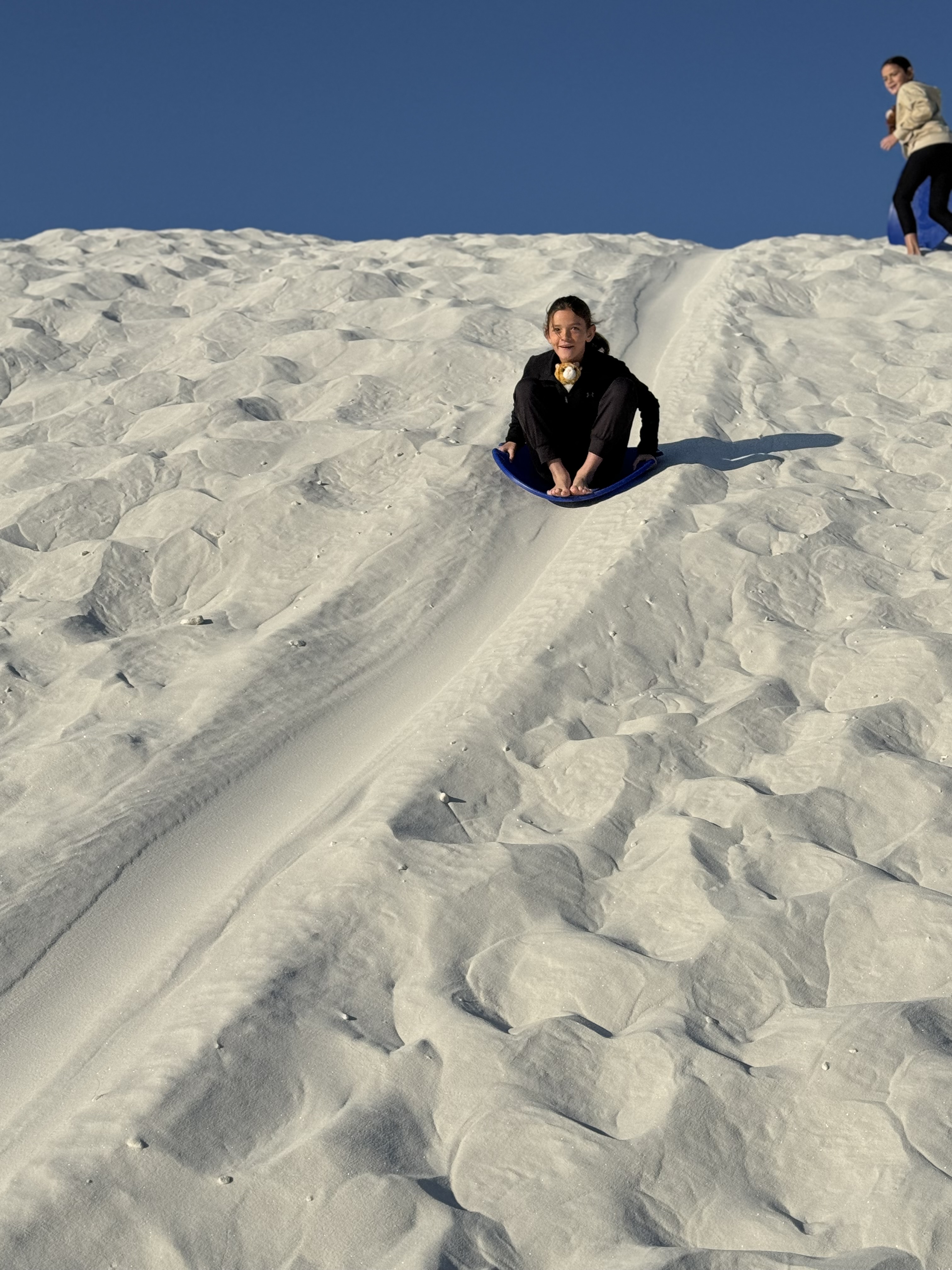 Child sledding down a white sand dune at White Sands National Park