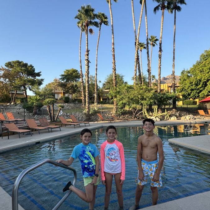 Kids enjoying a resort pool in Phoenix Arizona with palm trees and desert mountains