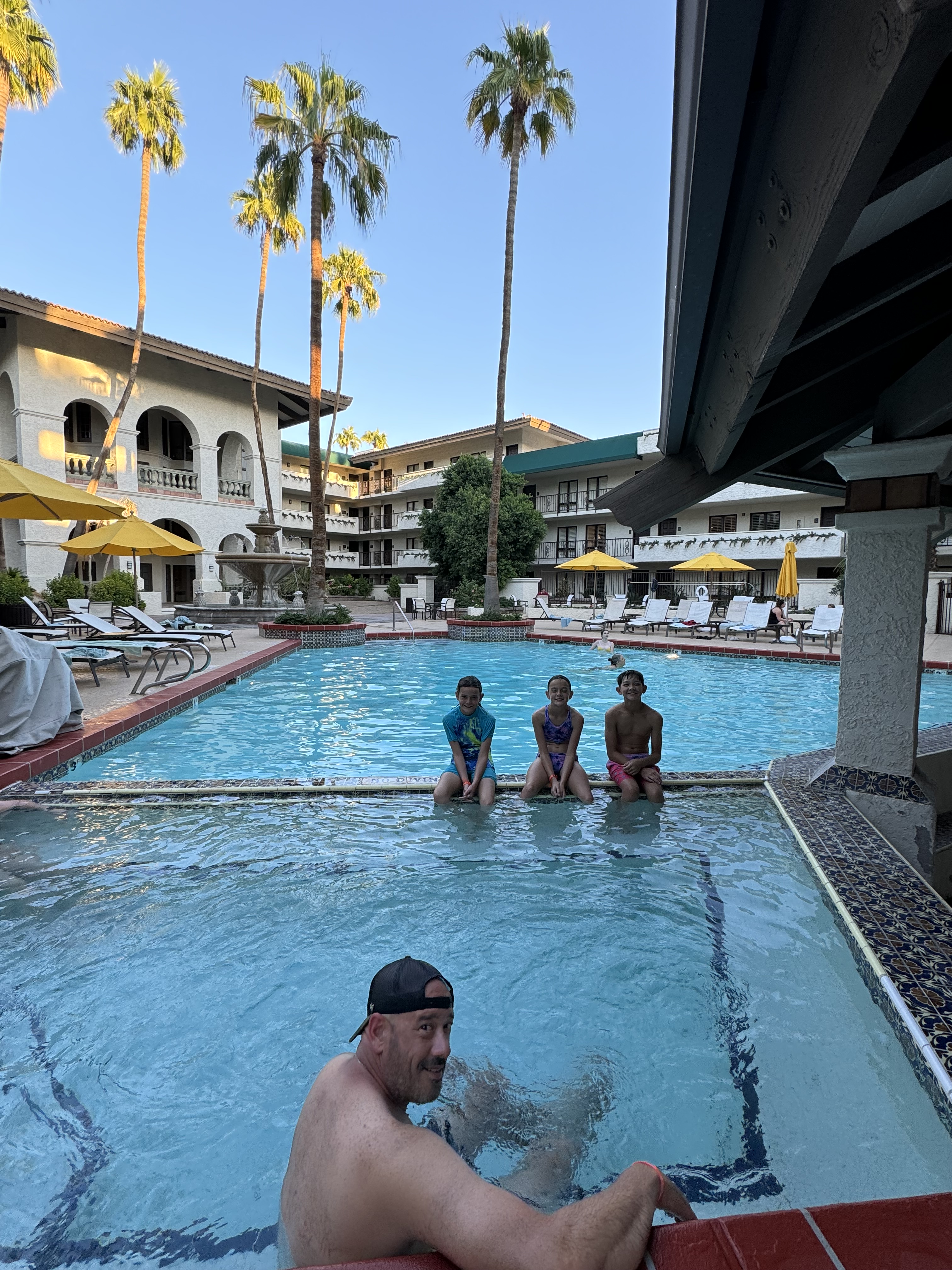 Family relaxing together in the Arizona Grand Resort pool with palm trees