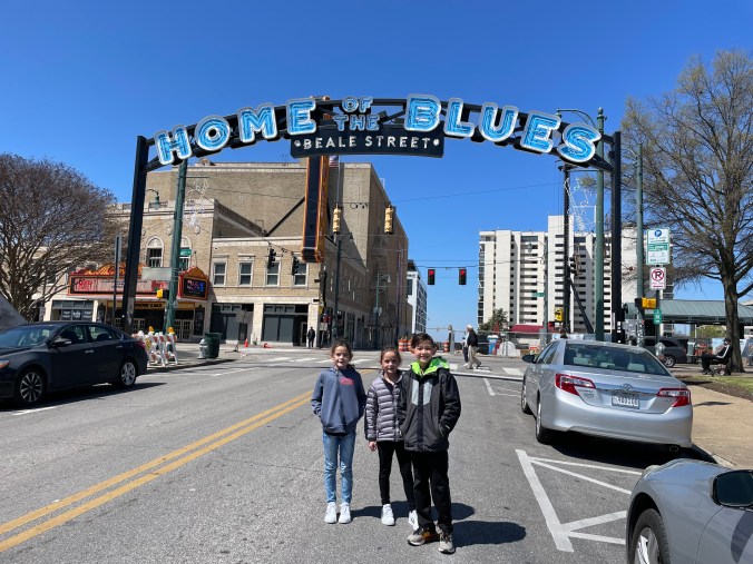 Kids standing beneath the Home of the Blues Beale Street sign in downtown Memphis Tennessee