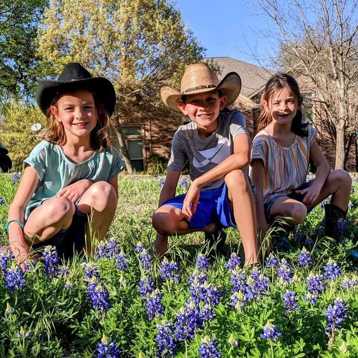 Kids wearing cowboy hats sitting in a Texas bluebonnet field during a spring family road trip