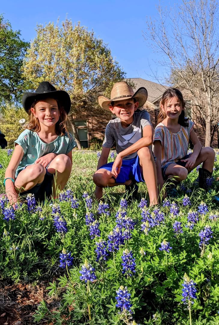 Kids sitting in Texas bluebonnets wearing cowboy hats during spring family road trip