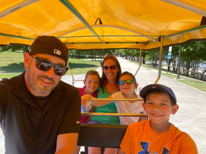 Family riding together in a pedal cart near the Big Four Bridge waterfront park in Louisville, Kentucky.