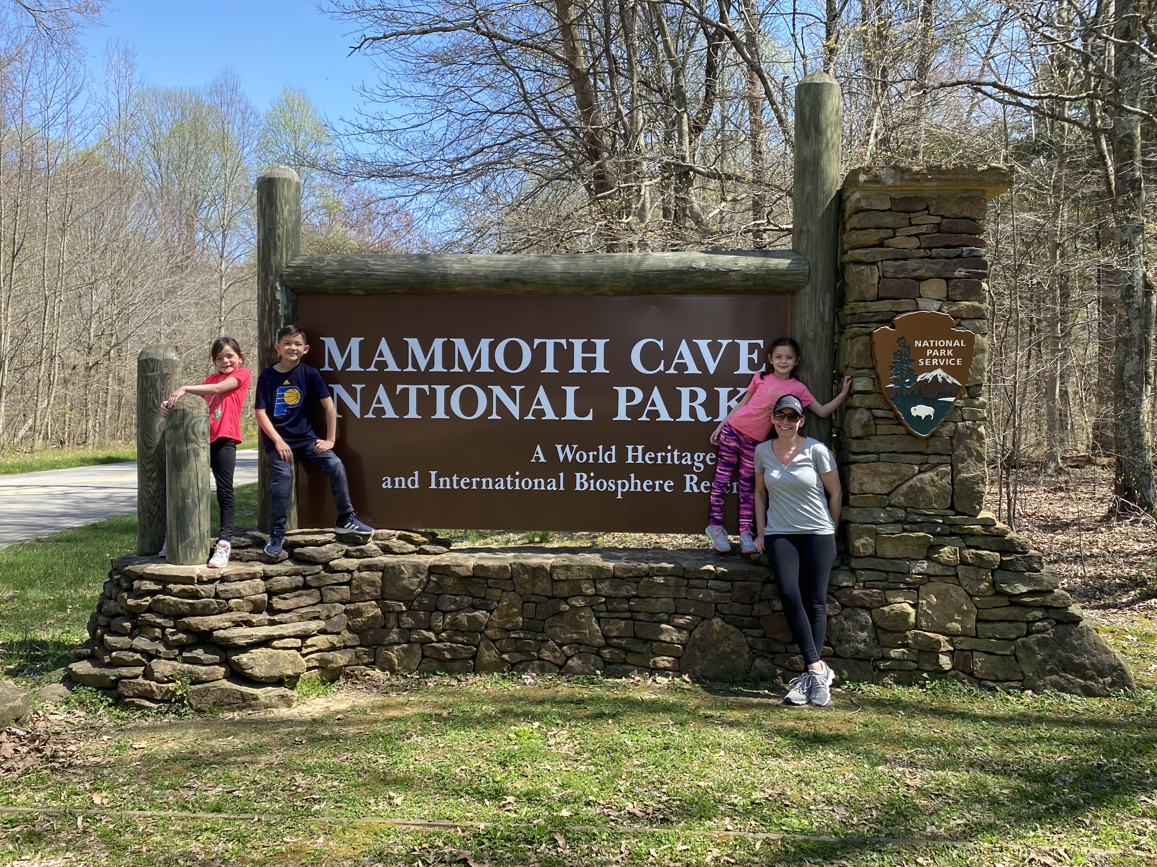 Family posing in front of the Mammoth Cave National Park sign during a Kentucky Georgia and Tennessee family road trip