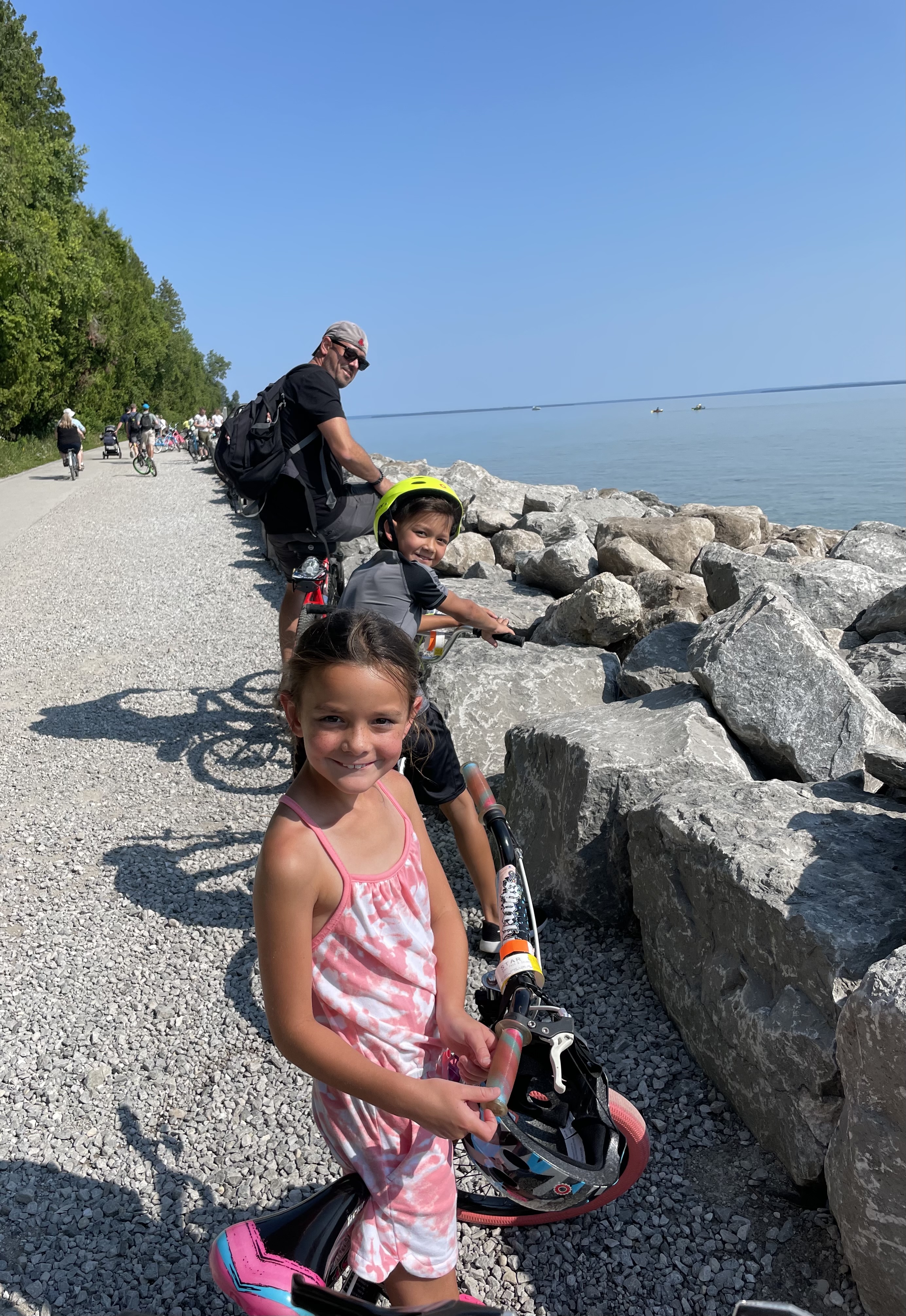Family biking on Mackinac Island near Lake Huron with clear water and rocks along the shoreline