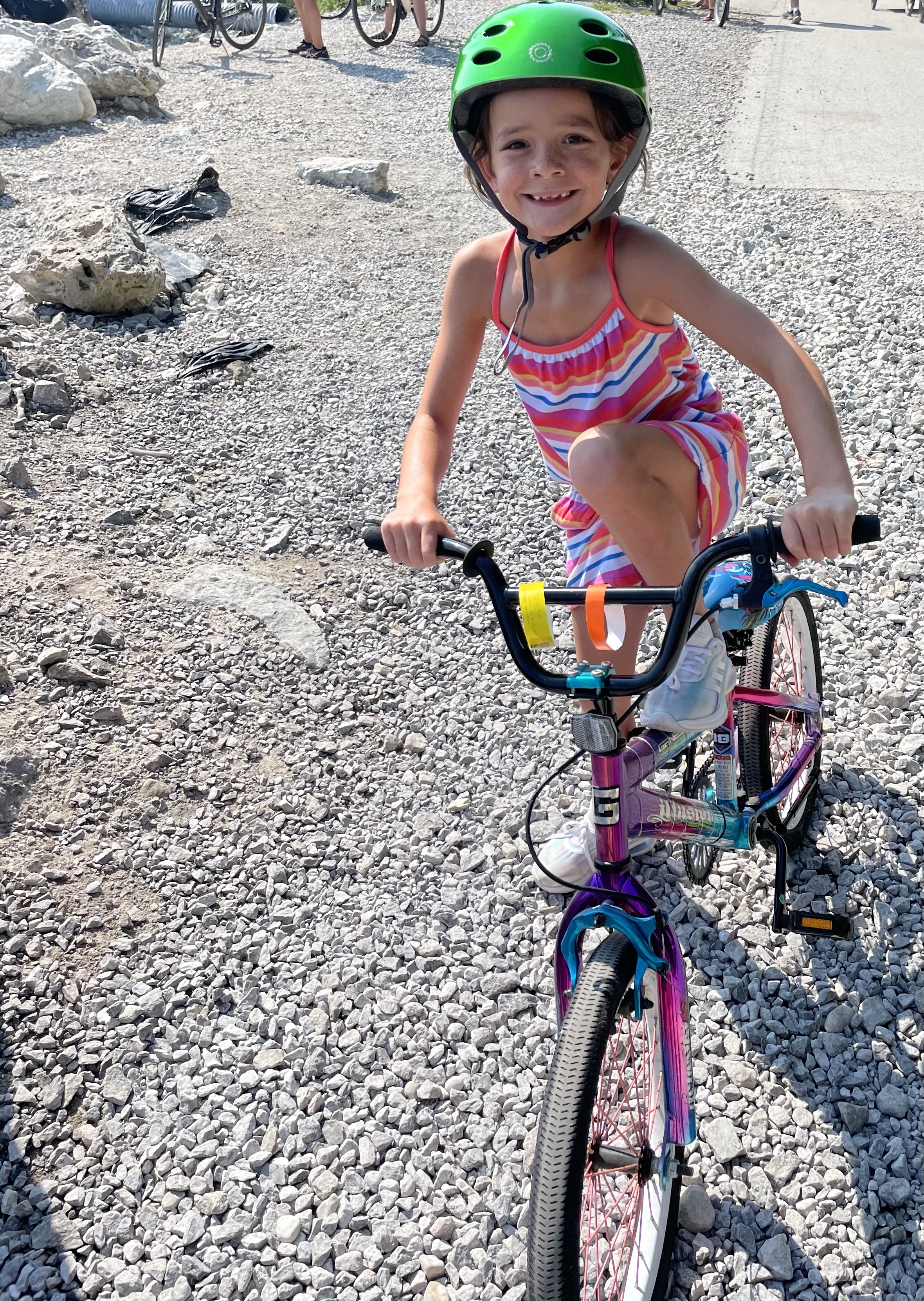 Young girl wearing a bright green helmet riding her bike along the rocky shoreline trail at Mackinac Island on a sunny summer day.