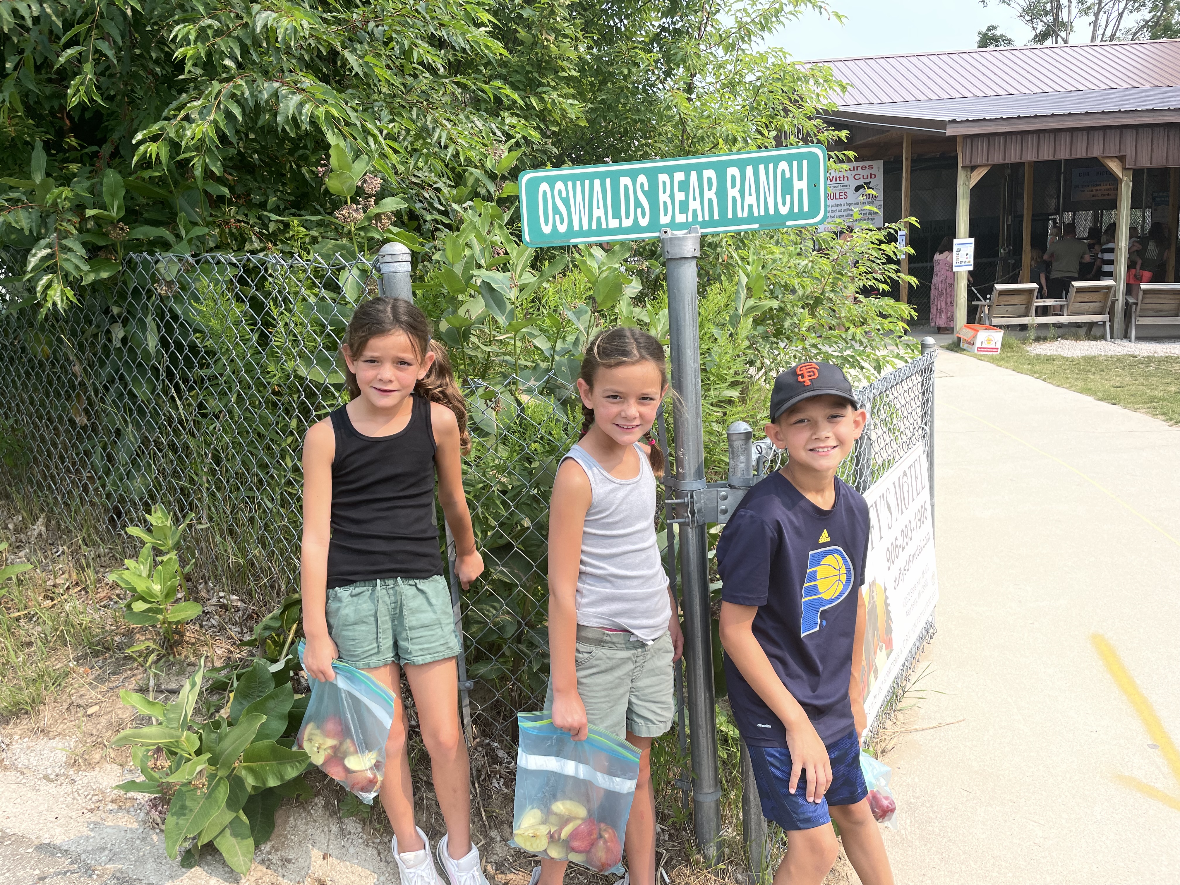 Kids standing near the Oswald's Bear Ranch sign in Michigan holding bags of apples