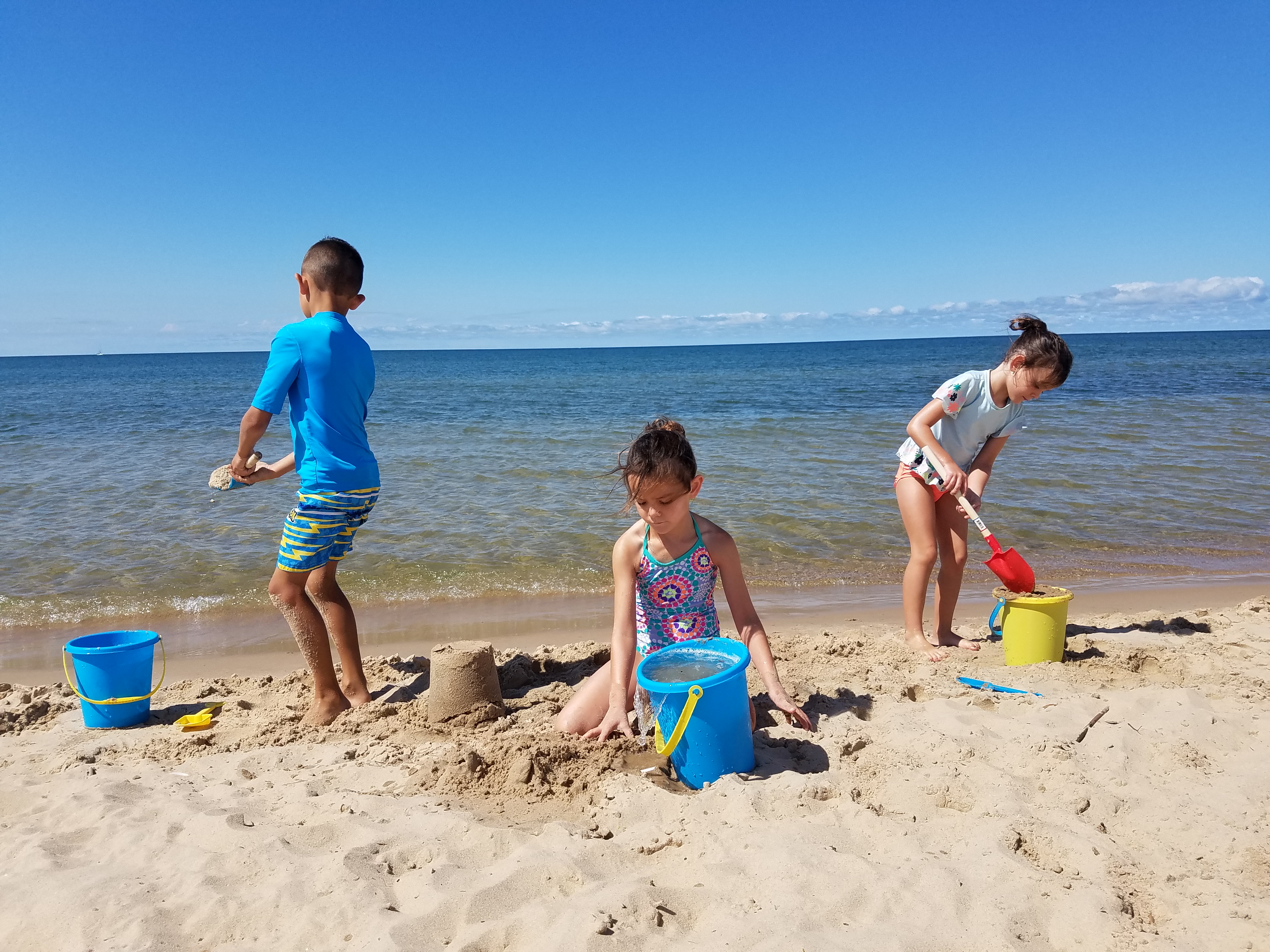 Three children building sandcastles and playing with beach buckets along Lake Michigan in Grand Haven, Michigan.