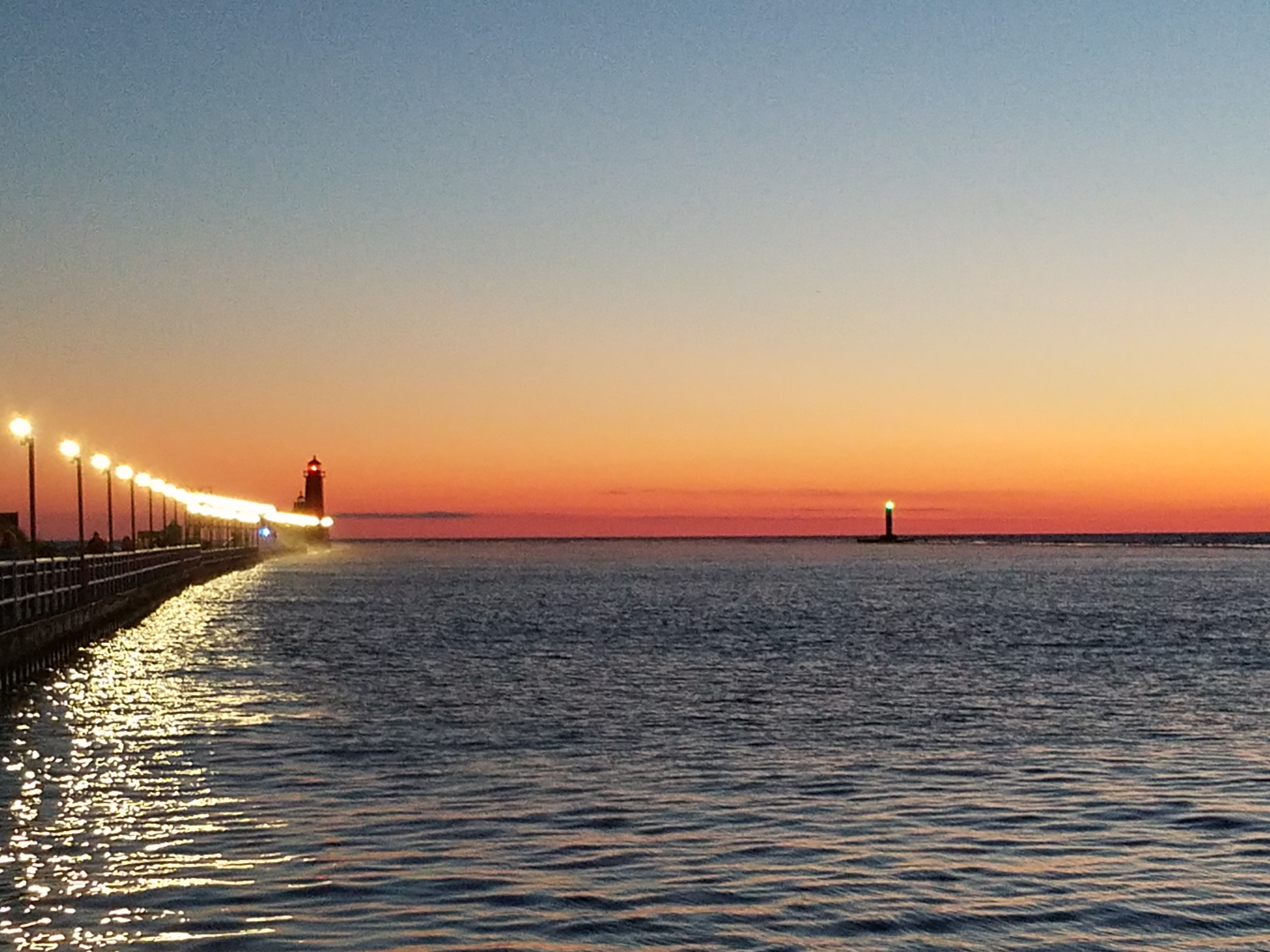 Grand Haven lighthouse and illuminated pier at sunset on Lake Michigan.