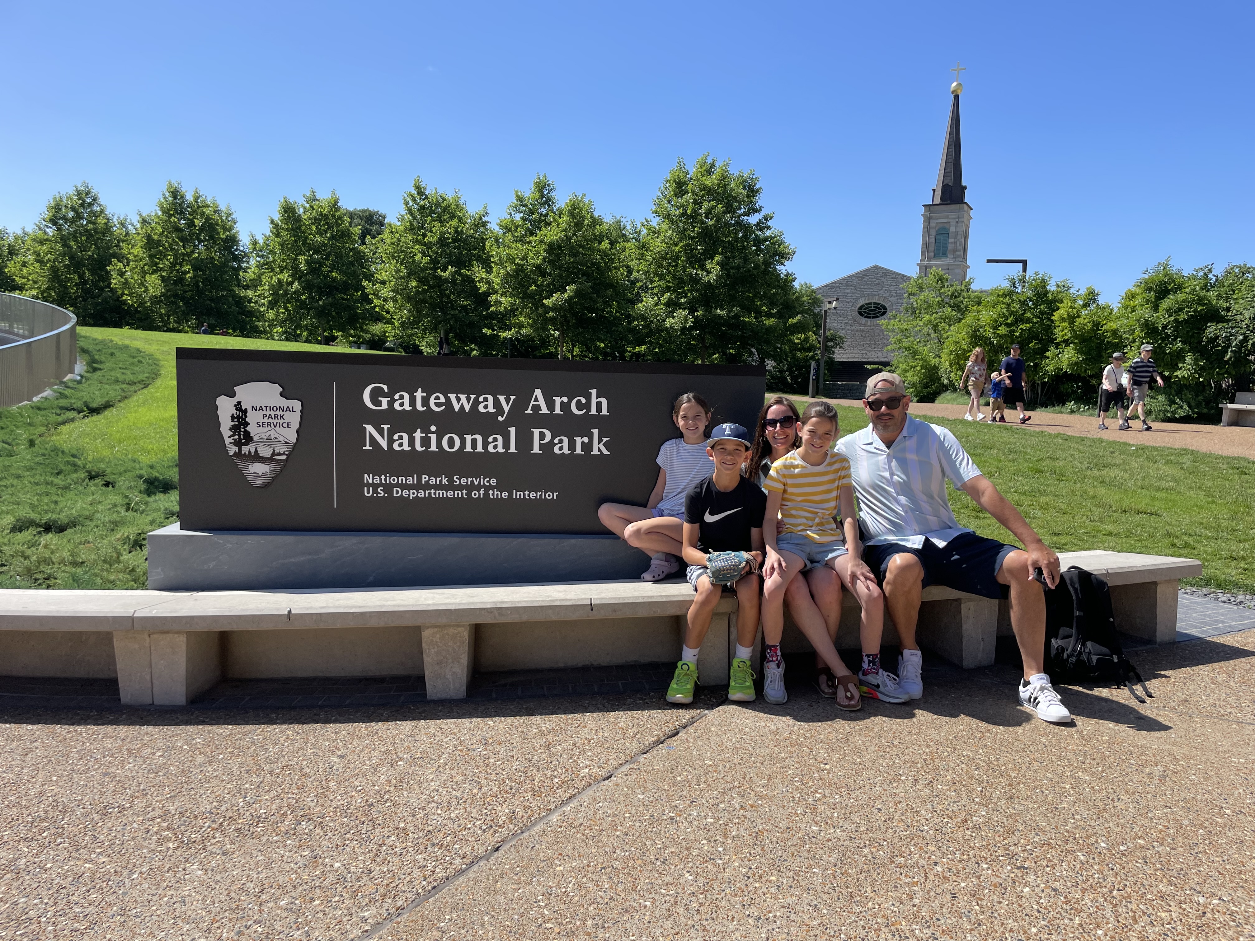 Family sitting by the Gateway Arch National Park sign in St. Louis Missouri